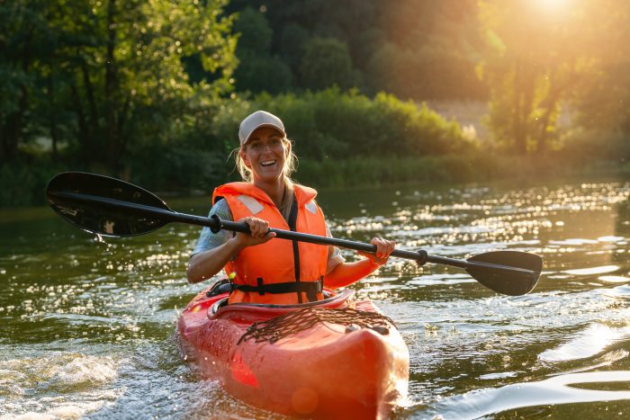 A woman kayaking on the river with trees behind her