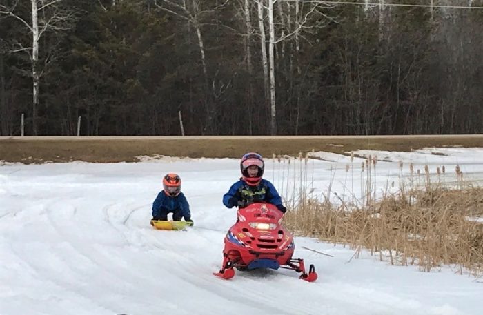 Kids snowmobiling on a trail